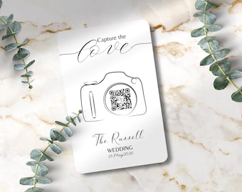 Puede incluir: Una tarjeta blanca con un dibujo lineal negro de una cámara y las palabras "Capture the Love". La tarjeta también incluye un código QR y el texto "The Russell WEDDING 15 May 2026".