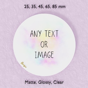 May include: A white circular sticker with the text "ANY TEXT OR IMAGE" in black. The sticker has a colorful, pastel-like design in the center. The text "25, 35, 45, 65, 85 mm" is above the sticker, and "Matte, Glossy, Clear" is below. The background is a textured lilac colour.