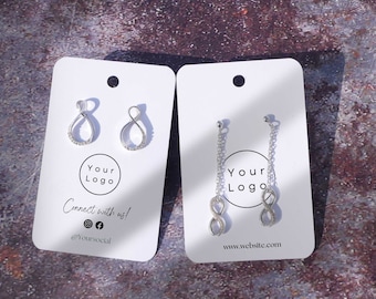 Puede incluir: Dos pares de pendientes de plata con símbolo de infinito en un cartón blanco con el texto "Your Logo" y "Connect with us!" con iconos de redes sociales y el texto "@Yoursocial".