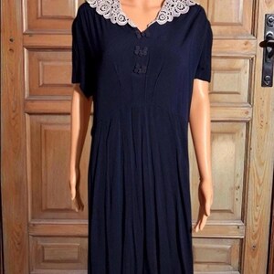May include: A navy blue dress with a white lace collar and short sleeves. The dress features decorative buttons and a pleated skirt. The dress is displayed on a mannequin.