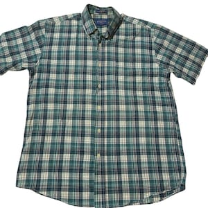 May include: A short-sleeve button-down shirt featuring a plaid pattern in shades of teal, navy blue, and off-white. The shirt includes a button-down collar, a single chest pocket, and a front button placket with a Pendleton brand label at the neck.