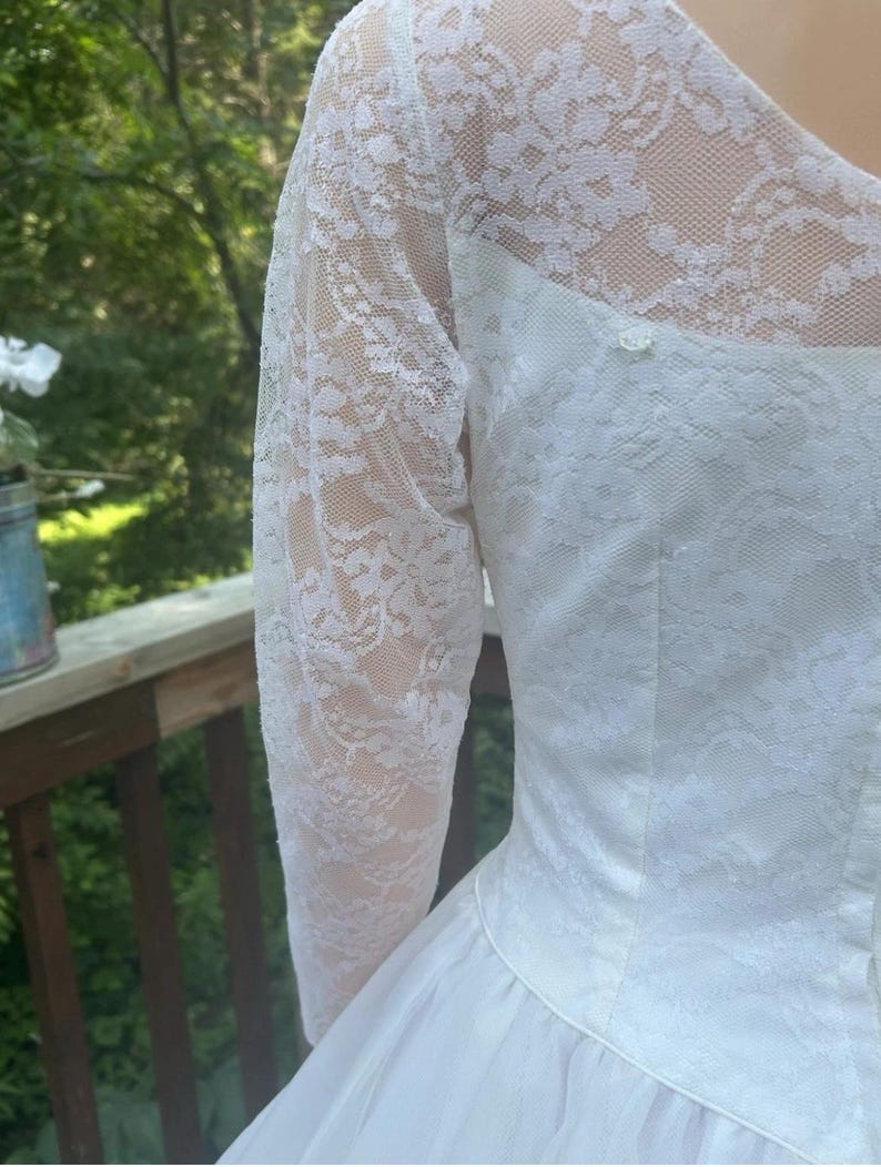 May include: White wedding dress with long lace sleeves. The bodice is fitted and the skirt flares out. The lace sleeves are sheer, and the dress appears to be made of a soft, flowing fabric. The dress is a classic style.