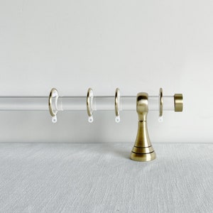 May include: A clear acrylic curtain rod with gold finials and rings. The rod is assembled and ready to be installed.