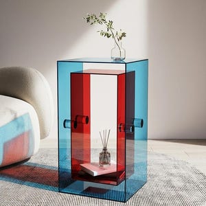 Könnte beinhalten: Ein rechteckiger Beistelltisch aus durchscheinenden blauen und roten Acrylplatten. Das Design zeichnet sich durch eine verschachtelte Struktur mit einem zentralen roten Teil aus, der von blauen Seitenteilen gehalten wird. Eine kleine Glasvase.