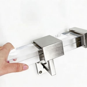 May include: A clear acrylic and brushed nickel curtain rod. The rod has a rectangular shape with a clear acrylic center and brushed nickel end caps and mounting hardware. The rod is designed for a modern aesthetic.