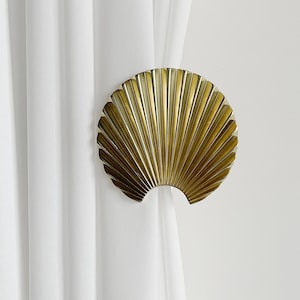 May include: Gold-toned metal curtain tieback shaped like a fan. The tieback is designed to hold back curtains or drapes.