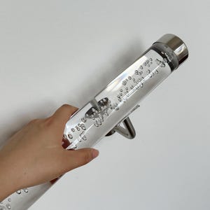 May include: A clear acrylic handrail with a silver bracket and many small bubbles inside. The handrail is mounted to a white wall.