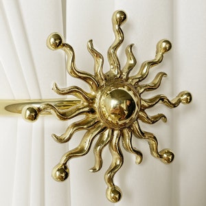May include: Gold-toned metal sun-shaped curtain tieback with a round center and wavy rays.