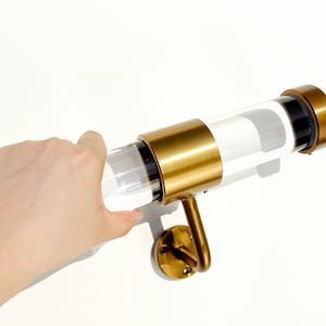 Puede incluir: Una barra de cortina de metal dorado con un tubo de acrílico transparente. La barra tiene un tapón de extremo decorativo y un soporte de pared.
