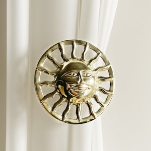 Puede incluir: Atado de cortina de sol dorado con una cara y rayos.