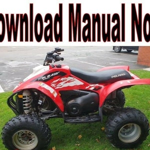 Puede incluir: Un ATV Polaris Trail Blazer rojo con asientos negros y detalles blancos. El ATV tiene cuatro ruedas y está estacionado en una superficie cubierta de hierba.