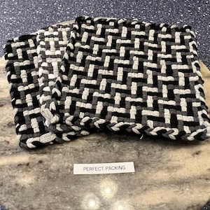 May include: Three black and white woven kitchen mats with a geometric pattern. The mats are stacked on top of each other and have a label that says "PERFECT PACKING".