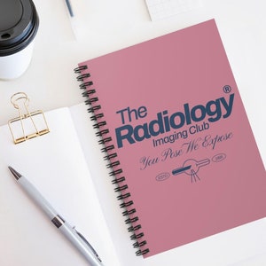 May include: A pink spiral bound notebook with the text "The Radiology Imaging Club You Pose We Expose" in navy blue lettering. The notebook also features a stylised illustration of an x-ray machine with the text "ESTD 1896" below it.