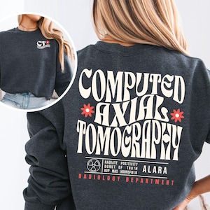 May include: Dark heather grey sweatshirt with a white graphic on the back that says "COMPUTED AXIAL TOMOGRAPHY" with a stylized flower on either side of the word "AXIAL". Below the graphic is a stylized radiation symbol with the text "RADIATE POSITIVITY DONUT OF TRUTH KVP MAS HOUNSFIELD ALARA RADIOLOGY DEPARTMENT".