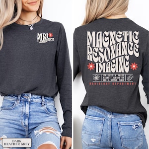 May include: Dark heather grey long-sleeved shirt with the text "MRI Technologist" on the front and "Magnetic Resonance Imaging" with a flower design on the back. The text on the back also includes "It's just a phase, magnet always on, add a little flair, Radiology Department."