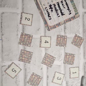 Könnte beinhalten: Eine Budget-Randomizer-Karte mit handgeschriebenen Kategorien wie "Taxes" und "Clothes" wird angezeigt. Mehrere kleine quadratische Karten mit Zahlen und Bücherregal-Designs sind um die Hauptkarte herum verstreut. Ein schwarzer Marker ist ebenfalls vorhanden.