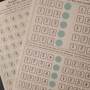 Könnte beinhalten: Zwei druckbare Spielbretter für das Spiel "Shut the Box". Die Bretter sind weiß mit schwarzen Zahlen und blauen Kreisen. Der Text "Budget Your Life" steht oben auf jedem Brett.