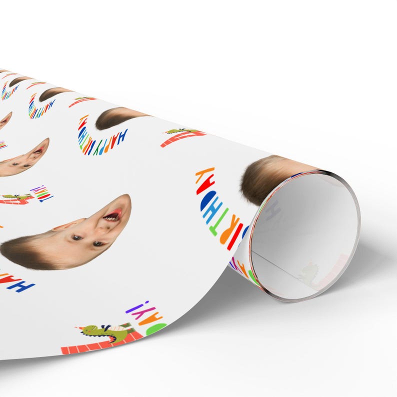 May include: A roll of white wrapping paper featuring a repeating pattern of a child's face, a green dinosaur illustration, and the text HAPPY BIRTHDAY in multi-colored letters. The design is printed on a smooth, matte-finish paper material.