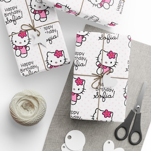 Puede incluir: Papel de regalo blanco con un patrón repetitivo de Hello Kitty con un conjunto rosa y una flor rosa, lunares de color rosa claro y el texto negro Happy Birthday Sofia. El papel está atado con cordel marrón y una etiqueta de estrella.