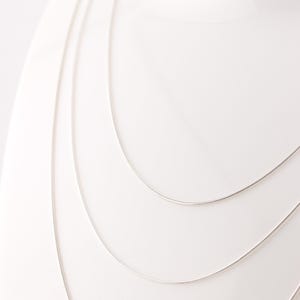 May include: Four silver chains of different lengths, layered on a white background.