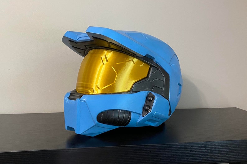 May include: A blue and gold plastic helmet with a visor. The helmet has a textured surface and a black trim around the visor.
