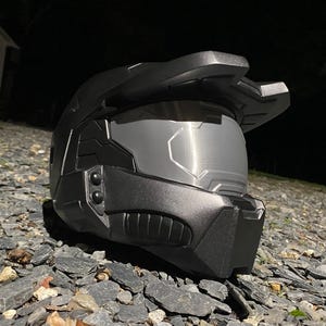 May include: A black helmet with a visor and a textured surface. The helmet has a design that resembles a futuristic soldier's helmet.