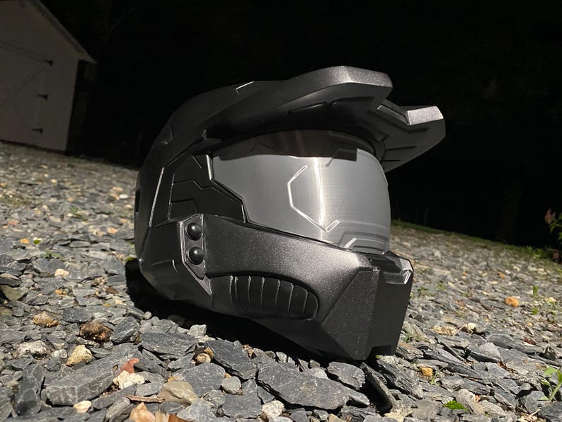 May include: A black helmet with a visor and a textured surface. The helmet has a design that resembles a futuristic soldier's helmet.