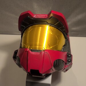 May include: A red and black helmet with a gold visor. The helmet has a textured surface and is made of plastic.