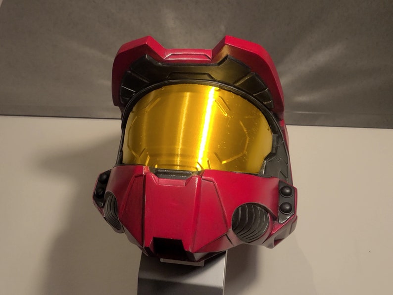 May include: A red and black helmet with a gold visor. The helmet has a textured surface and is made of plastic.