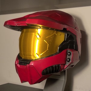 May include: A red and black helmet with a gold visor. The helmet has a textured surface and a raised design on the front.