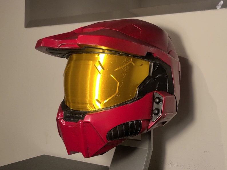 May include: A red and black helmet with a gold visor. The helmet has a textured surface and a raised design on the front.