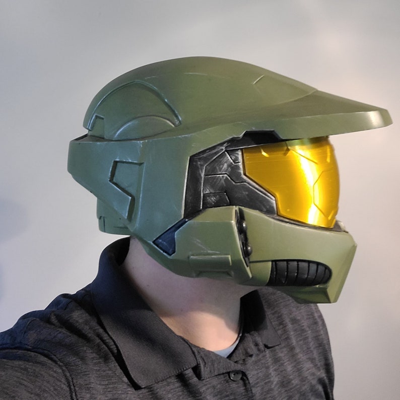May include: A green and black plastic helmet with a gold visor. The helmet has a textured surface and a raised design.
