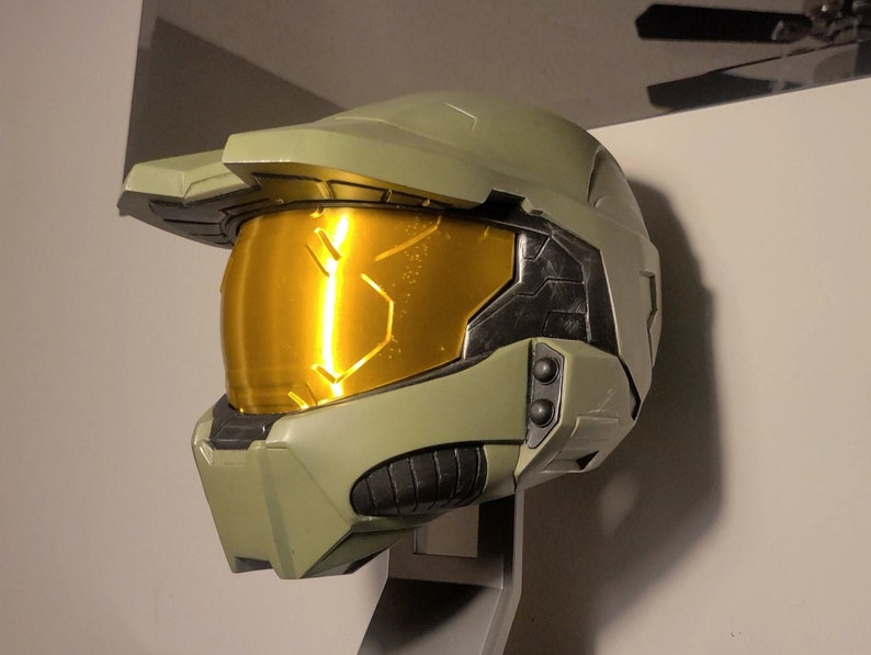 May include: A green and gold Master Chief helmet from the Halo video game series. The helmet has a visor and a black detail on the side.