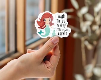 May include: A white sticker featuring a cartoon mermaid with red hair and a teal tail. The mermaid is holding a small bottle. Text on the sticker reads, "I WANT TO BE WHERE THE PEOPLE AREN'T."