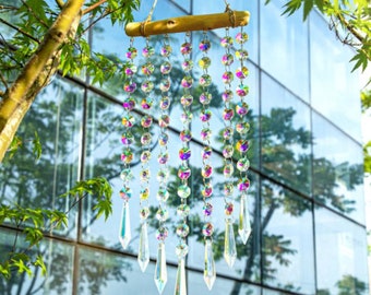 May include: A crystal prism wind chime with iridescent beads hanging from a wooden dowel. The chime is suspended from a string and is hanging in front of a window.