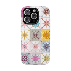 May include: A patterned phone case featuring a patchwork design with floral motifs in various colors. The case has a white background with squares of pink, yellow, blue, and green flowers. The phone case has a black camera and side buttons.
