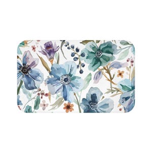 May include: Rectangular bath mat featuring a watercolor floral pattern. The design includes blue, teal, and purple flowers with green leaves and brown stems on a white background. The mat has rounded corners.