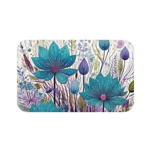 May include: A rectangular bath mat featuring a watercolor floral design. The mat showcases large turquoise flowers with purple centers, surrounded by various green and purple foliage against a white background. The design has a soft, artistic aesthetic.