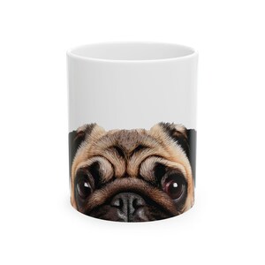 May include: White ceramic mug with a brown and black pug face peeking over the rim. The pug's eyes are wide open and its nose is visible.
