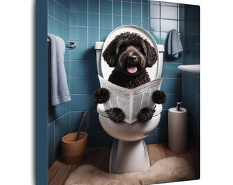 May include: A black curly-haired dog sits on a white toilet in a blue-tiled bathroom, holding an open newspaper with both front paws. The dog has its tongue out, and the bathroom features a hanging gray towel and a wooden waste bin.