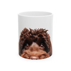 May include: A white ceramic mug with a brown dog's face peeking over the rim. The dog has brown fur and dark eyes.