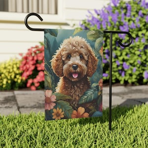 May include: A garden flag featuring a brown and white doodle dog with a pink tongue sticking out. The dog is surrounded by green leaves and colorful flowers.
