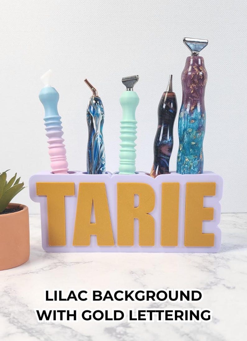 May include: A lilac-colored holder with gold lettering that spells "TARIE" holds five razors with colorful handles. The razors have blue, pink, green, and marbled designs. The text "LILAC BACKGROUND WITH GOLD LETTERING" is at the bottom.