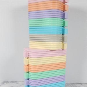 May include: Stacked, colorful, pastel-colored foam blocks. The blocks are arranged in a rectangular shape, with each layer a different color, including pink, orange, yellow, green, blue, and gray. The blocks have rounded edges.