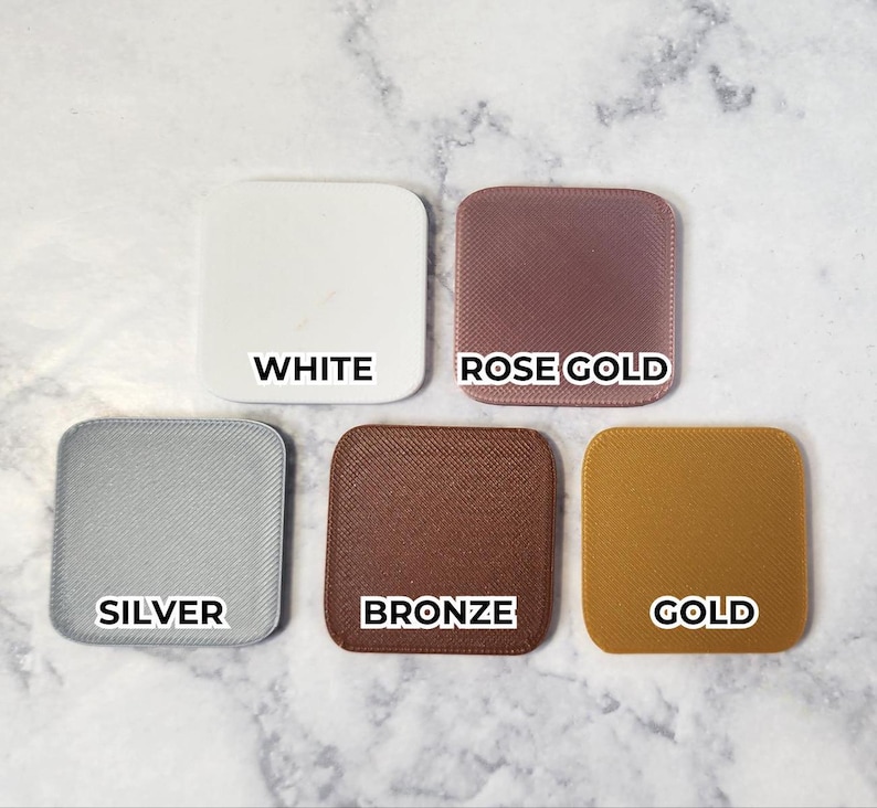 May include: Five square color swatches in white, rose gold, silver, bronze, and gold. Each swatch has rounded corners and a textured surface. The color names are printed in black, centered on each swatch.