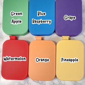 May include: Six colorful, rectangular containers with rounded corners are displayed. Each container is a different color: green, blue, purple, red, orange, and yellow. Each container has a label with a fruit name: Apple, Raspberry, Grape, Watermelon, Orange, and Pineapple.