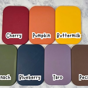 May include: A collection of seven rectangular color swatches with rounded corners. The colors include cherry red, pumpkin orange, buttermilk yellow, spinach green, blueberry blue, taro purple, and pecan brown. Each swatch has a white label with the color name.