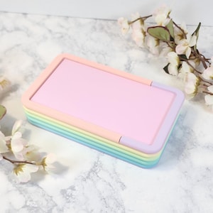 May include: A rainbow-colored stackable storage box with a light pink lid. The box is made of plastic and has a smooth, glossy finish.
