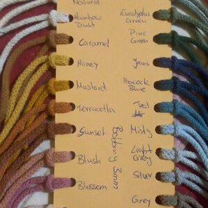 May include: A color chart featuring various shades of cord, with names like "Natural," "Blossom," and "Blackberry." The cords are attached to a yellow card with handwritten color names. The cords are 3mm thick.