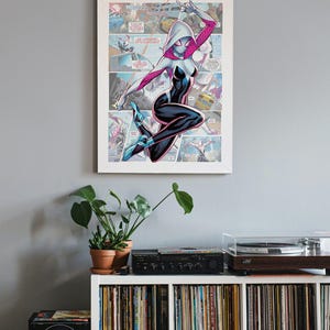 May include: A white and pink Spider-Gwen comic book character illustration with a white mask and black suit. The character is posed in mid-air with her arms raised and a web line attached to her wrist. The illustration is set against a comic book panel background.